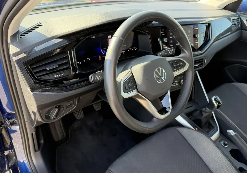Vue intérieure côté conducteur du Volkswagen Taigo bleu, volant cuir multifonction et levier de vitesse manuel visible.