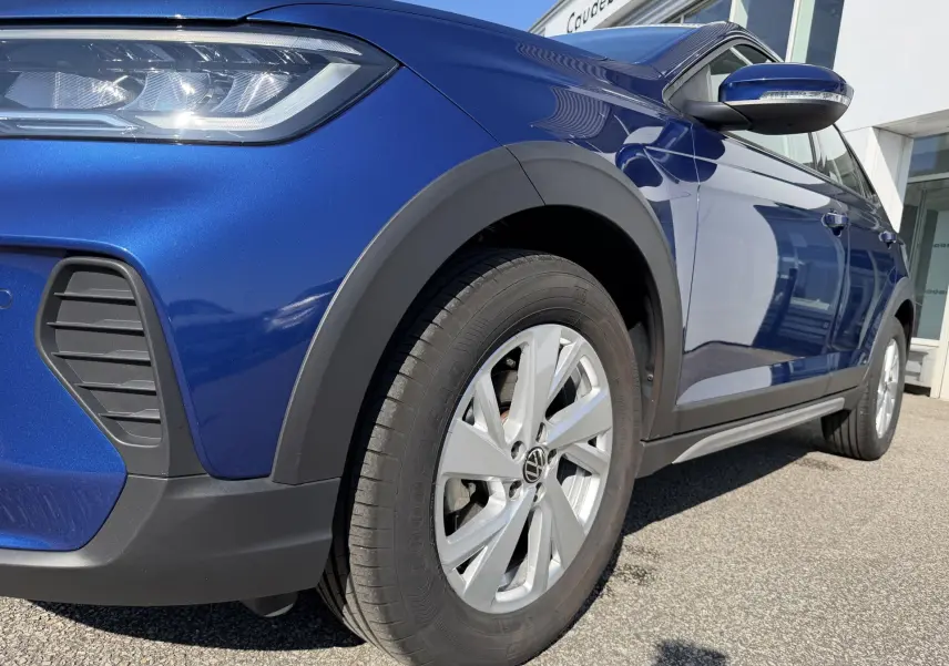 Vue 3/4 avant droit du Volkswagen Taigo bleu métallisé avec jantes alliage et protections plastiques noires.