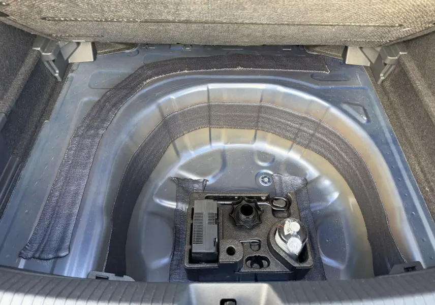 Vue plongeante sur le coffre ouvert d’un Volkswagen Taigo bleu, montrant le compartiment à outils et kit de dépannage.