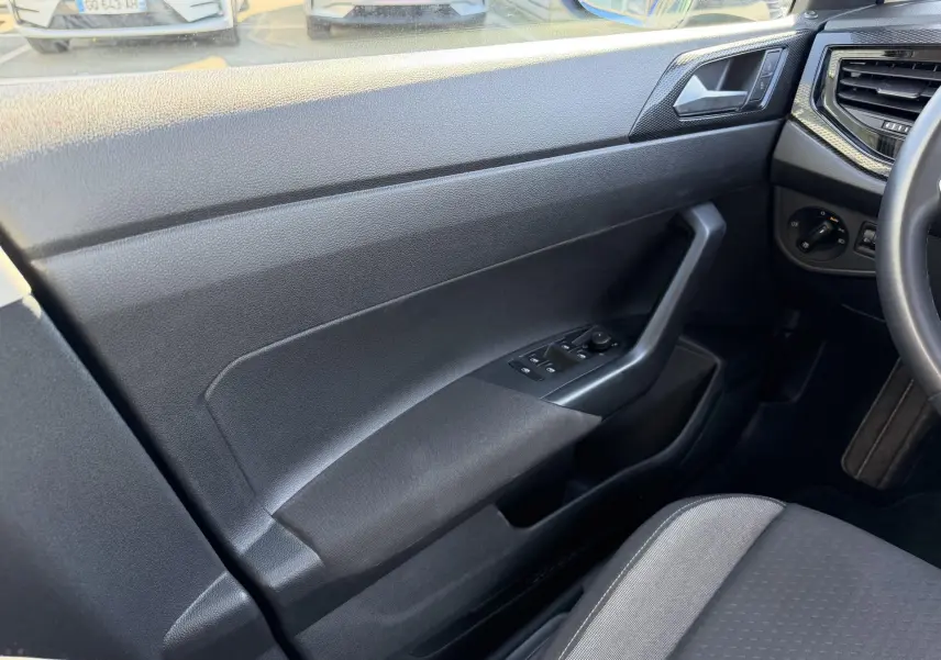 Intérieur côté conducteur du Volkswagen Taigo 2025, montrant la portière noire avec commandes des vitres et partie du siège tissu gris.
