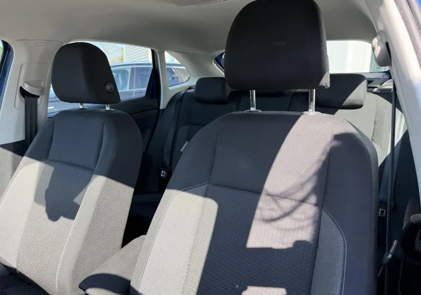 Vue intérieure rapprochée des sièges avant en tissu gris du Volkswagen Taigo bleu, avec appuie-têtes et ceinture de sécurité visibles.