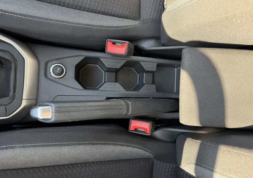 Vue plongeante sur la console centrale noire du Volkswagen Taigo 2025 avec frein à main manuel et porte-gobelets.