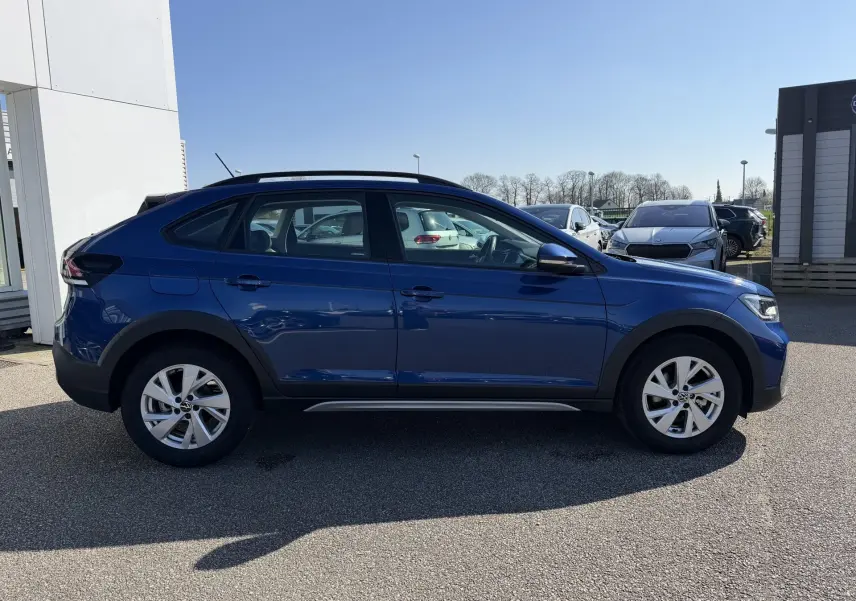 Vue de profil côté gauche d'un Volkswagen Taigo 2025 bleu métallisé avec jantes alliage et barres de toit noires.