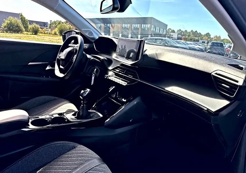 Vue intérieure côté conducteur de la Peugeot 208 1.2 100 Allure avec tableau de bord noir et écran tactile central.
