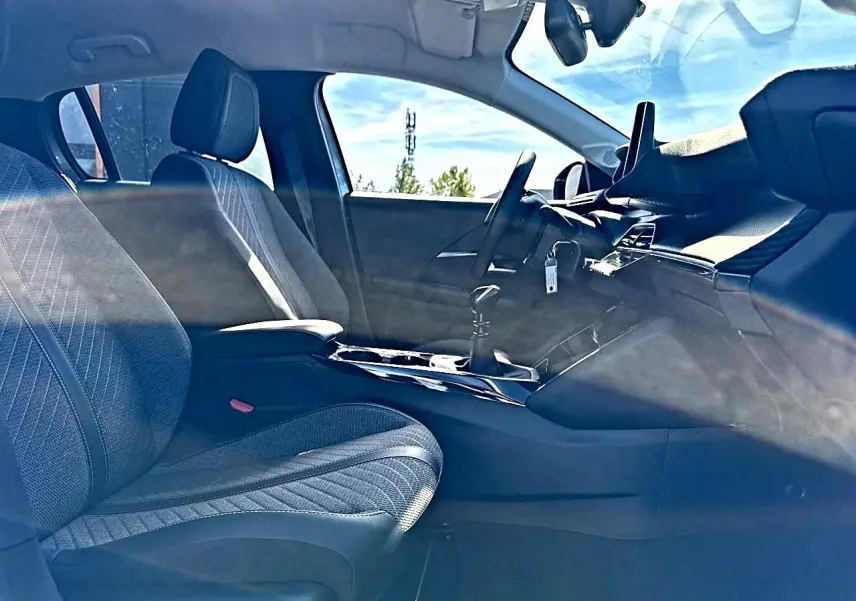 Vue intérieure côté conducteur de la Peugeot 208 1.2 100 allure avec sièges tissu gris et tableau de bord moderne.