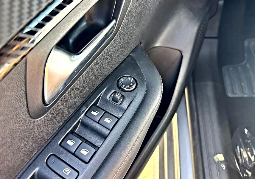 Gros plan sur la commande des vitres électriques côté gauche de la porte avant d'une Peugeot 208 gris Artense.