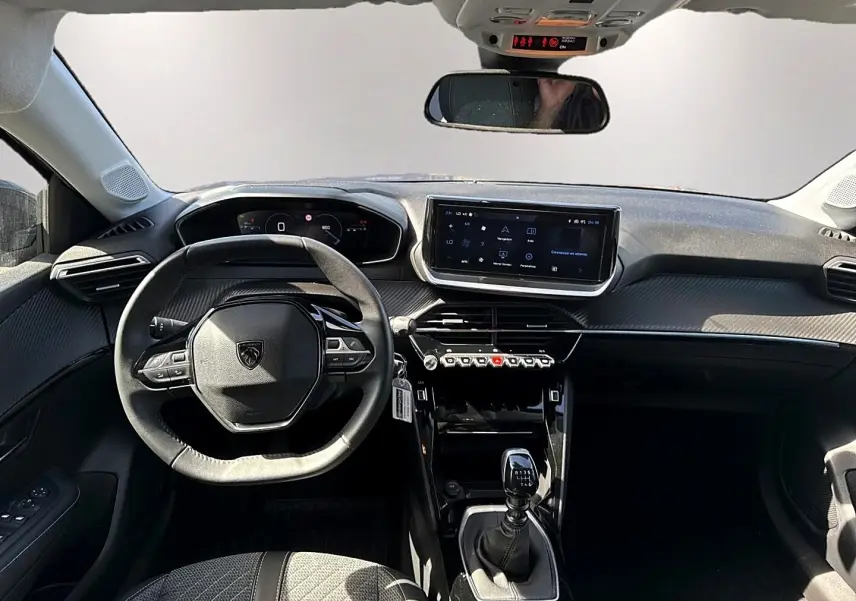 Vue intérieure frontale du poste de conduite de la Peugeot 208 1.2 100 allure, volant compact et écran tactile central.