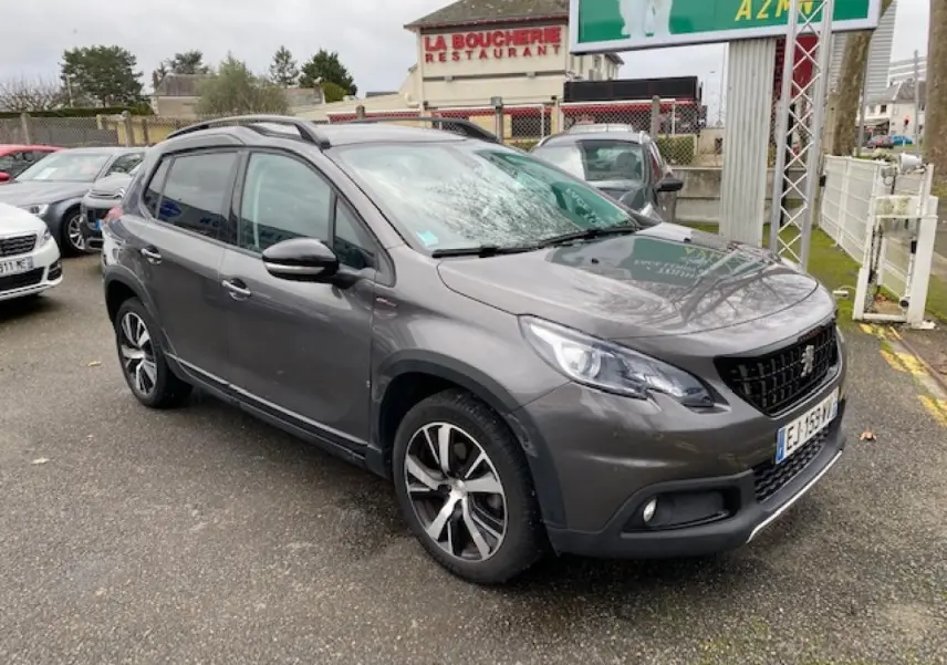 Peugeot 2008 gris foncé vue 3/4 avant droit, avec jantes alliage 17 pouces et barres de toit noir brillant.