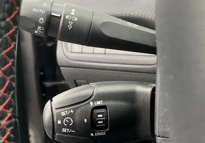 Gros plan sur la commande de régulateur de vitesse du Peugeot 2008 gris foncé, avec volant en cuir noir et surpiqûres rouges.