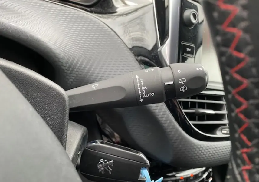 Gros plan sur la commande d’essuie-glace et la clé Peugeot dans l’habitacle noir du 2008 gris foncé.