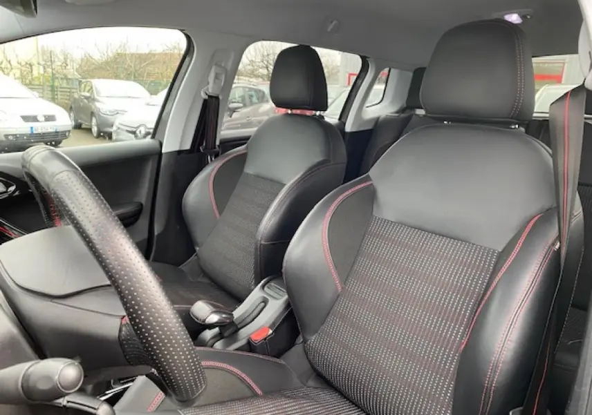 Intérieur de la Peugeot 2008 gris foncé, vue sur les sièges avant en cuir noir avec surpiqûres rouges et volant perforé.