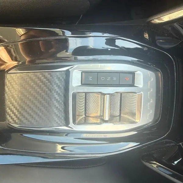 Vue rapprochée de la console centrale noire brillante du Peugeot 208 Hybrid 110 e-DCS6 Allure 2024 avec sélecteur de vitesses automatique.