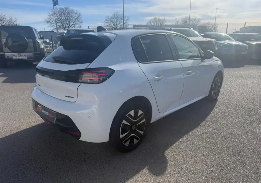 Vue 3/4 arrière droite d'une Peugeot 208 Hybrid blanche 2024 avec jantes distinctives et feux arrière noirs.