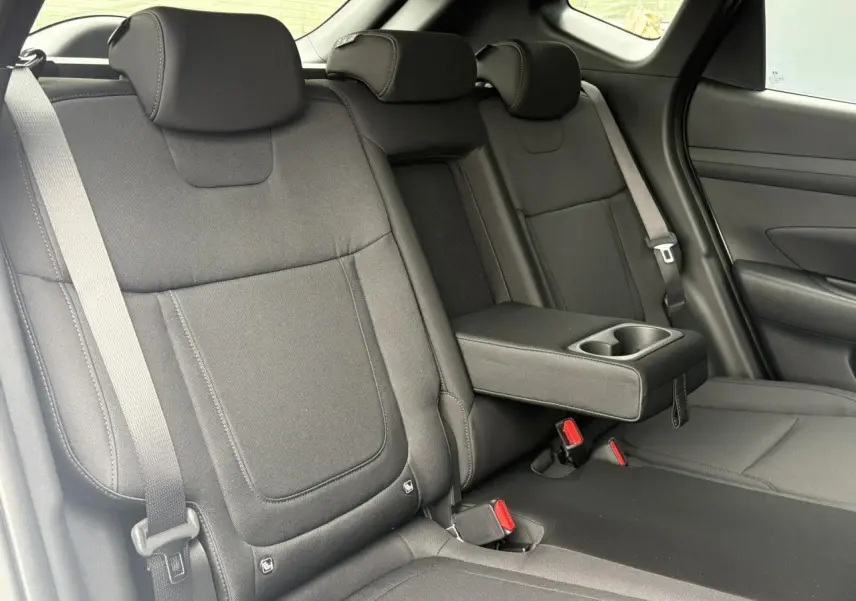 Vue intérieure sur les sièges arrière noirs du Hyundai Tucson 2026 avec accoudoir central et ceintures visibles.