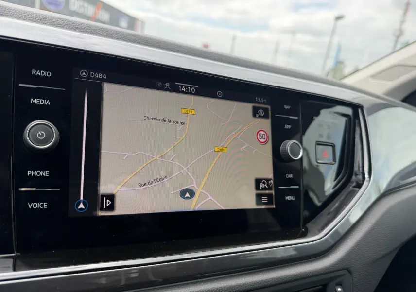 Vue rapprochée de l'écran tactile de navigation du tableau de bord de la Volkswagen Polo 2025, avec commandes latérales visibles.