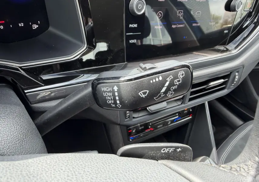 Gros plan sur la commande d’essuie-glace dans l’habitacle noir d’une Volkswagen Polo bleue, avec écran tactile en arrière-plan.