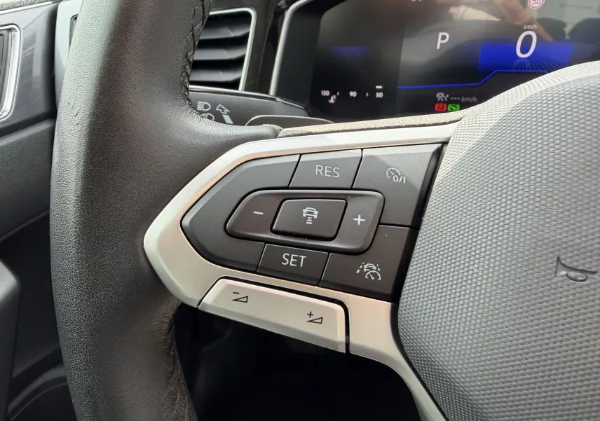 Gros plan sur le volant cuir de la Volkswagen Polo 2025 avec commandes du régulateur adaptatif et affichage digital en arrière-plan.