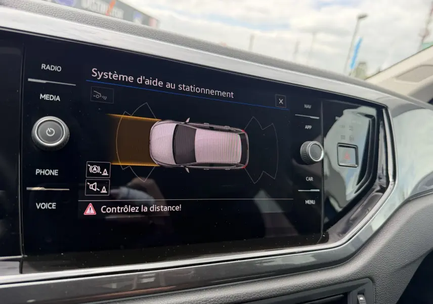 Écran tactile intérieur montrant l'aide au stationnement d'une Volkswagen Polo 2025, vue de face côté conducteur.
