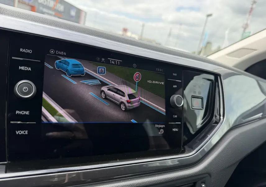 Écran tactile intérieur montrant l’aide au stationnement avec vue 3/4 arrière d’une Volkswagen Polo bleue.