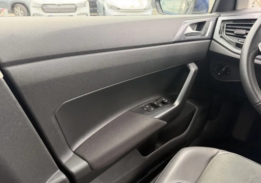Vue intérieure côté gauche de la porte avant d'une Volkswagen Polo 2025 avec commandes de vitres et garniture noire.
