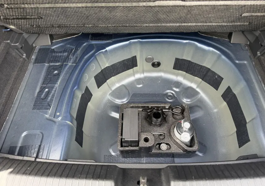 Vue plongeante sur le coffre ouvert d'une Volkswagen Polo bleue 2025, montrant le rangement sous plancher métallique.