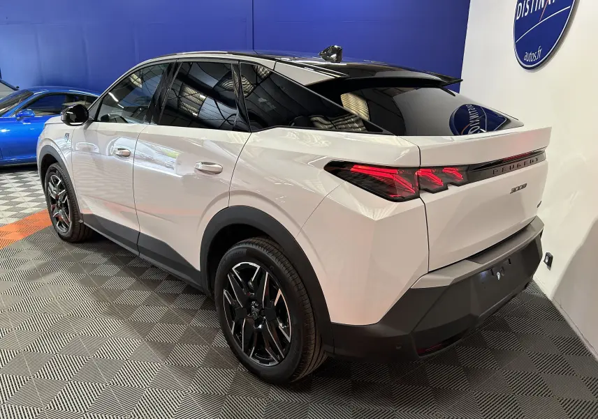 Vue 3/4 arrière droite d’un Peugeot 3008 blanc Okenite avec toit noir et jantes noires en intérieur showroom.