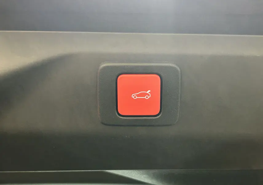 Bouton rouge d'ouverture électrique du hayon sur le coffre d'un Peugeot 3008 blanc Okenite 2025.