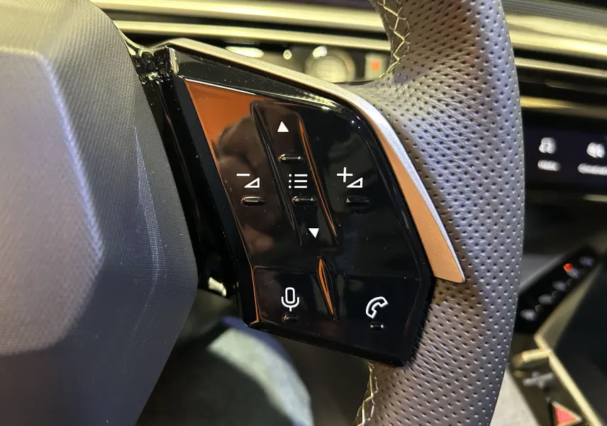 Gros plan sur les commandes tactiles noires du volant perforé du Peugeot 3008 blanc Okenite, version hybride 2025.