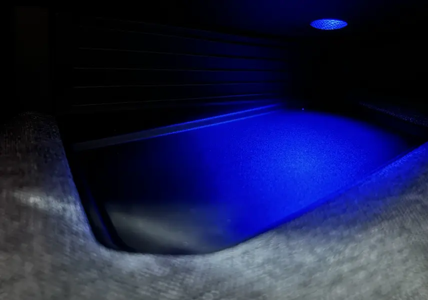Gros plan intérieur sur le compartiment de rangement éclairé en bleu du Peugeot 3008 Hybrid blanc Okenite.
