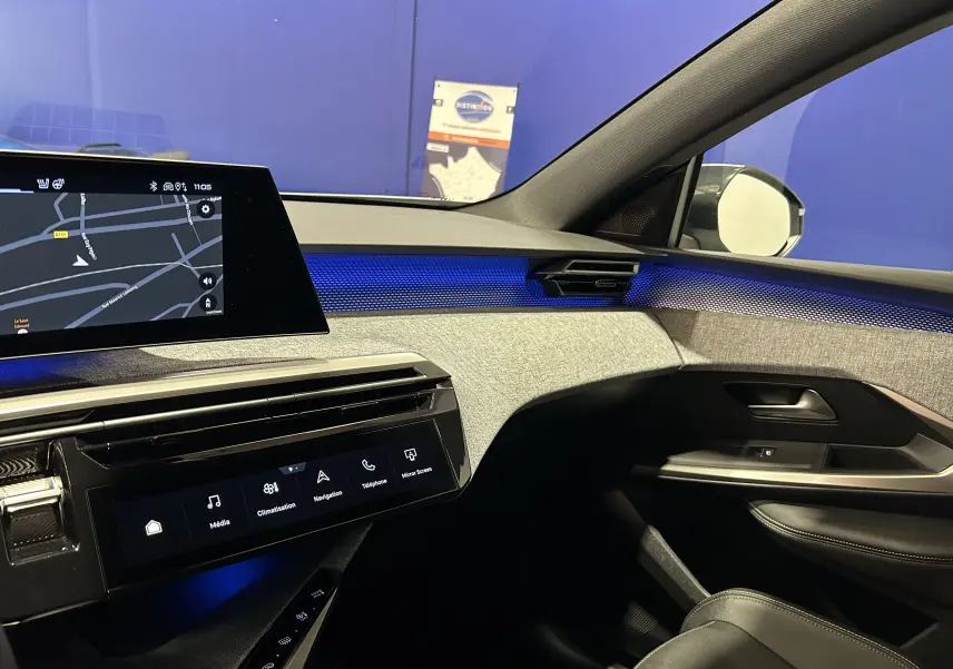 Vue intérieure côté passager du Peugeot 3008 Hybrid 2025, avec éclairage d'ambiance bleu et écran tactile de navigation.
