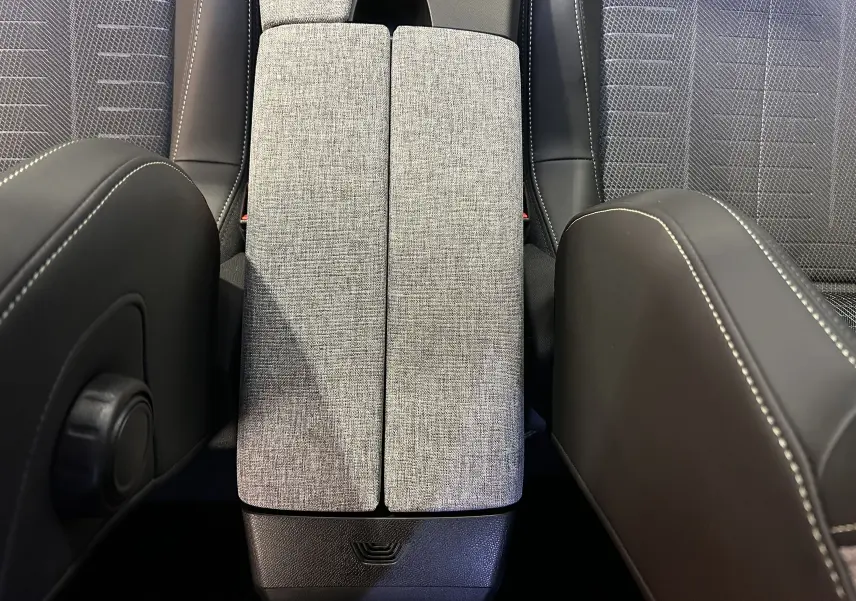 Vue plongeante sur la console centrale en tissu gris et sièges noirs avec surpiqûres blanches du Peugeot 3008 Hybrid 2025.