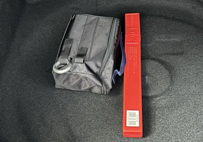 Coffret de secours noir et triangle de signalisation rouge posés sur le tapis de coffre d’un véhicule.