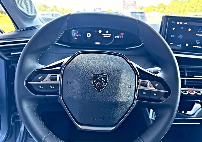 Vue rapprochée du volant noir de la Peugeot 208 1.2 100 Allure avec tableau de bord numérique et écran tactile.