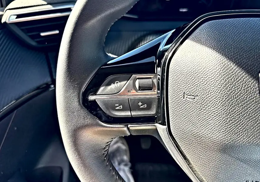 Gros plan sur le volant noir de la Peugeot 208 1.2 100 Allure, montrant les commandes audio et téléphone à gauche.