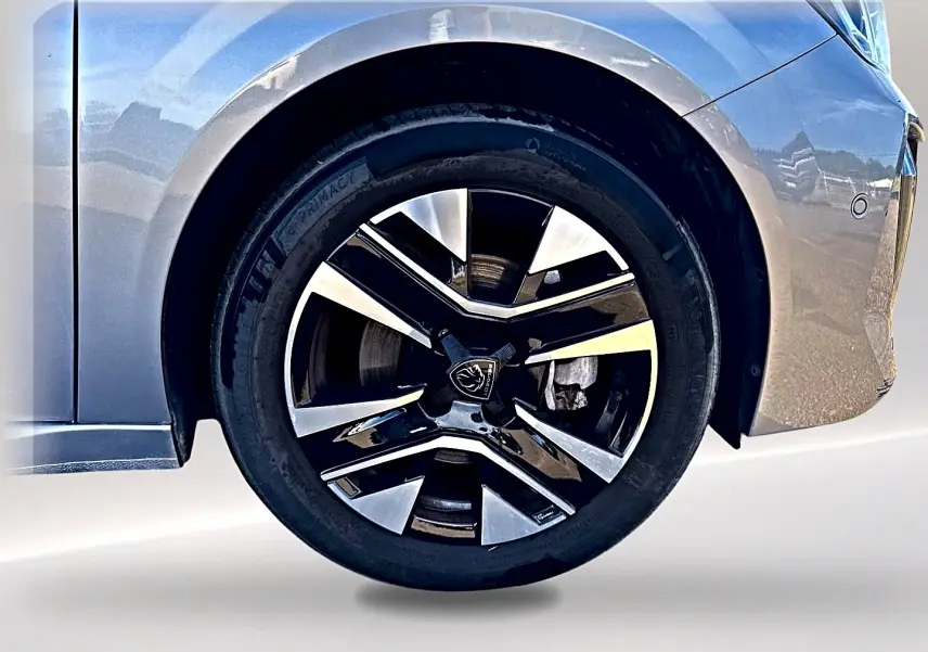 Gros plan sur la roue avant droite de la Peugeot 208 1.2 100 Allure gris Artense avec jante alu bicolore.