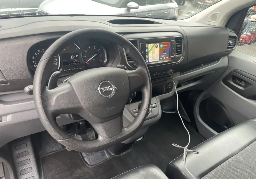 Vue intérieure côté conducteur de l'Opel Vivaro Fourgon 2020, tableau de bord noir avec écran tactile et volant multifonction.