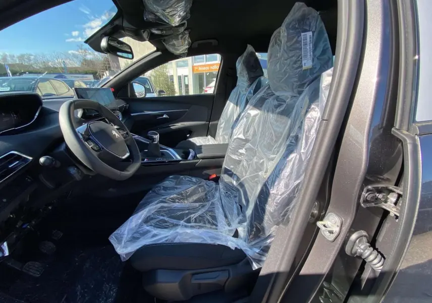 Intérieur avant droit du Peugeot 5008 gris platinium 2023 avec sièges protégés par film plastique.