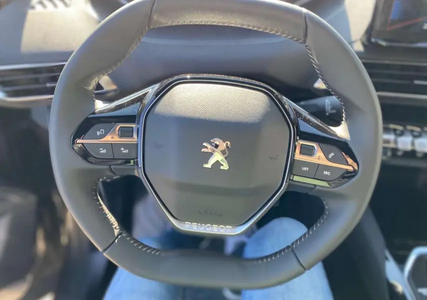 Vue rapprochée du volant compact multifonctions du Peugeot 5008 2023 avec logo lion chromé au centre.