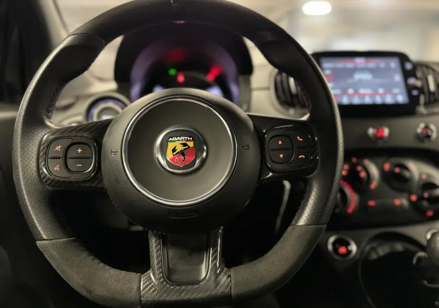 Volant cuir/alcantara avec logo Abarth au centre, tableau de bord et écran tactile 7'' vus de face à l'intérieur du véhicule.