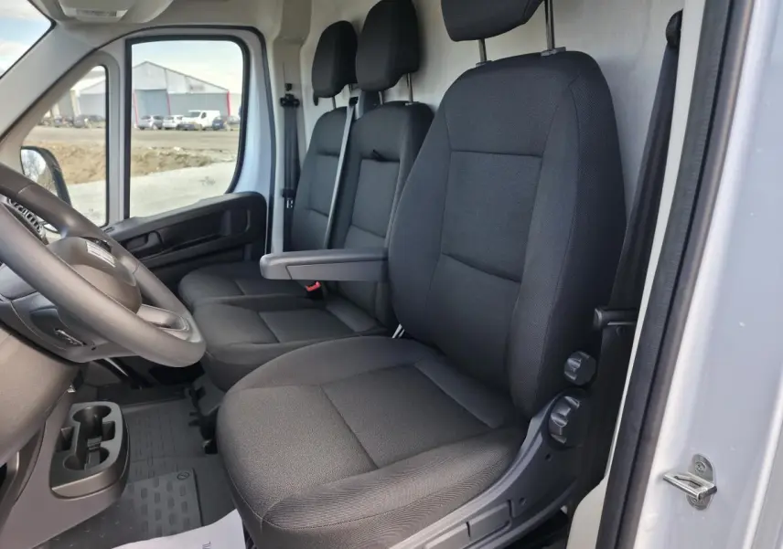Vue intérieure côté conducteur du Fiat Ducato Fourgon blanc, montrant les sièges en tissu noir et le volant.
