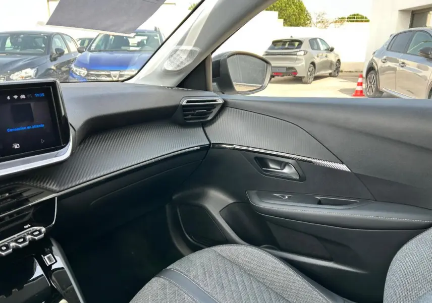 Vue intérieure côté passager de la Peugeot 208 Hybrid 110 e-DCS6 Allure 2024 avec tableau de bord gris et sièges tissu.