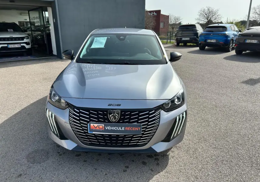 Vue avant d'une Peugeot 208 gris métallisé 2024 avec calandre noire et feux LED verticaux distinctifs.
