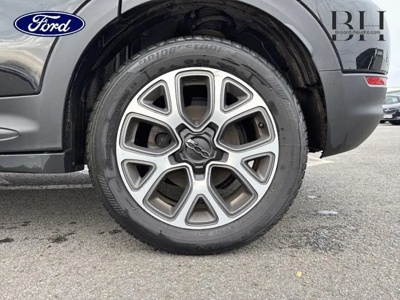 Gros plan sur la roue avant droite noire d'une FIAT 500X 2017 avec jante alu distinctive et pneu Bridgestone.