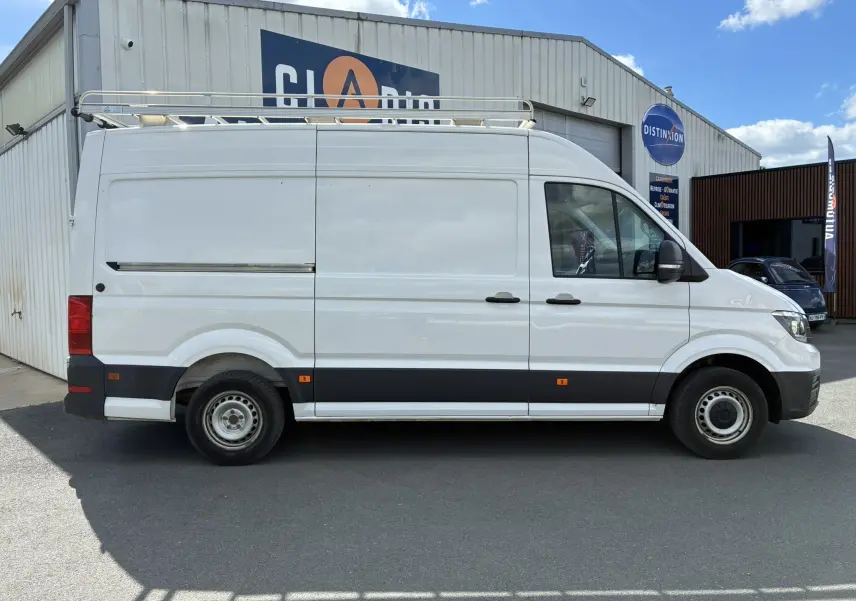 Vue de profil côté droit d'un Volkswagen Crafter blanc avec galerie de toit et double portes arrière ouvertes à 270° visibles en arrière-plan.