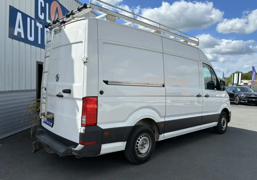 Vue 3/4 arrière droite d'un Volkswagen Crafter blanc avec galerie de toit et échelle métallique arrière.