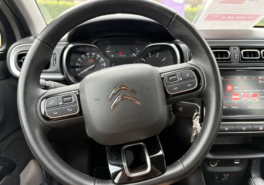 Vue rapprochée du volant noir de la Citroën C3 beige 2019 avec commandes intégrées et tableau de bord visible.