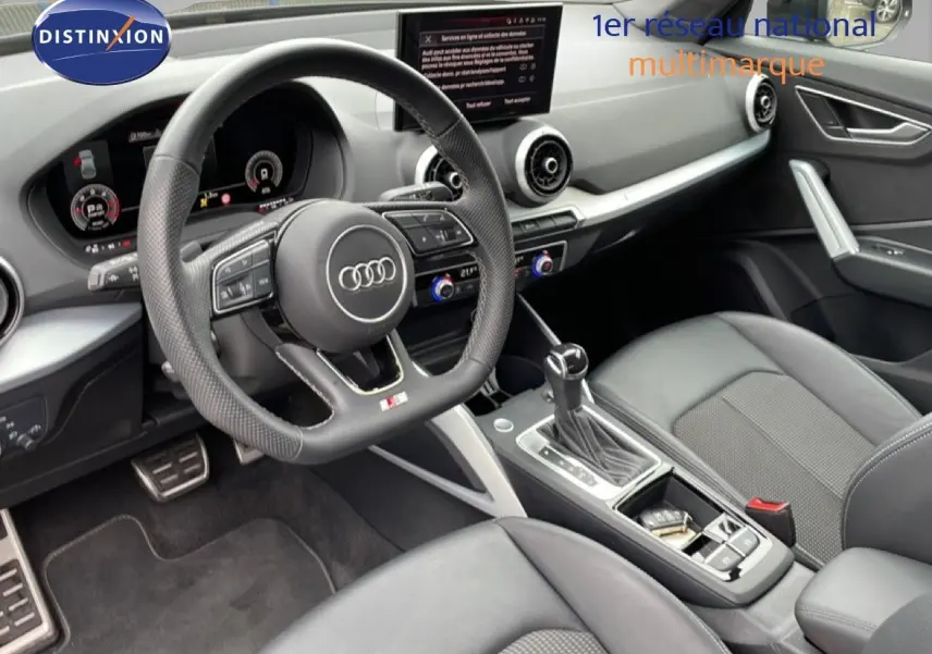 Vue intérieure de l'Audi Q2 35 2.0 TDI S-Line 2025, mettant en valeur le volant cuir perforé et la console centrale moderne.