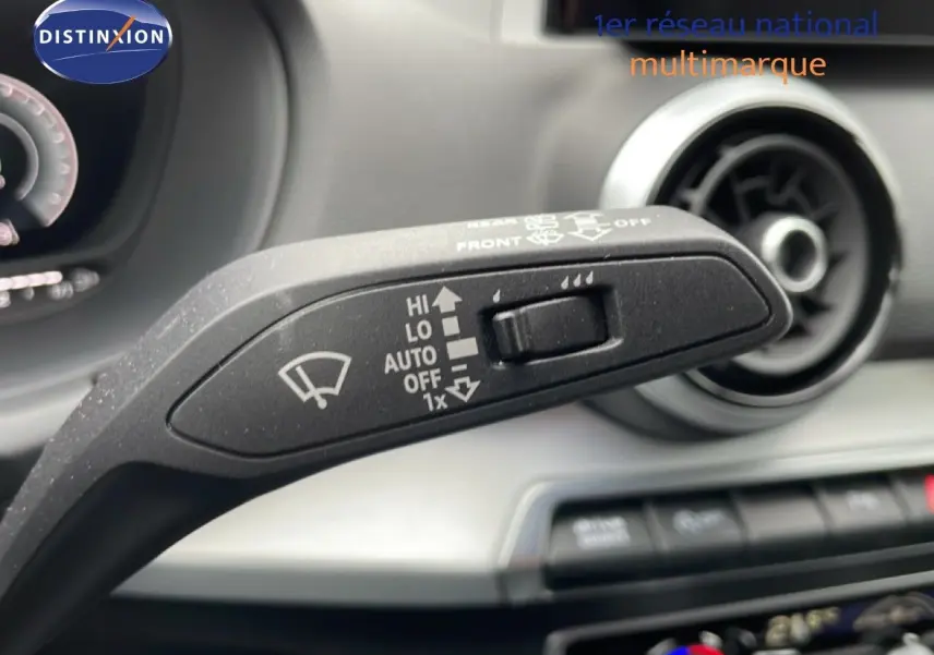 Gros plan sur la commande d’essuie-glace dans l’habitacle d’un Audi Q2 noir mito metal, avec tableau de bord et aérateurs visibles.