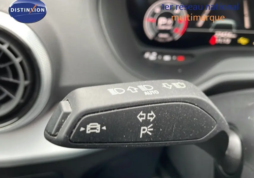 Gros plan sur la commande de clignotant et feux d'un Audi Q2 noir mito metal, intérieur avec tableau de bord flou en arrière-plan.