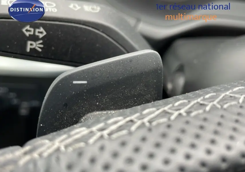Gros plan sur la palette de changement de vitesse derrière le volant en cuir perforé de l'Audi Q2 noir mito metal.